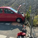 Ein Auto steht mit offener Motorhaube an einem Bauzaun.