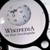 Unter einer Lupe ist der Schriftzug und das Logo des Online-Lexikons Wikipedia auf einem Computerbildschirm zu sehen.