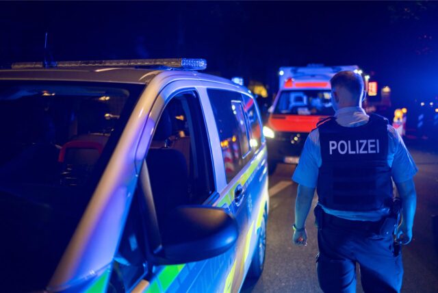 Ein Polizist steht nachts während eines Einsatzes auf dem Stadtfest in Unna neben einem Streifenwagen. Im Hintergrund ist ein Rettungswagen.