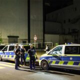 Polizeibeamte stehen mit Polizeifahrzeugen vor einem Gebäude in Iserlohn.