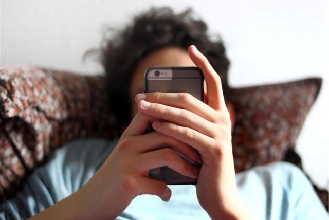 Ein junger Mann blickt auf ein Smartphone.