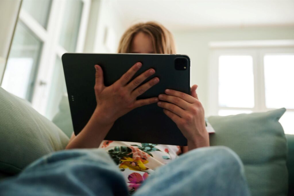 Ein Mädchen sitzt auf der Couch und guckt auf ein Tablet. 