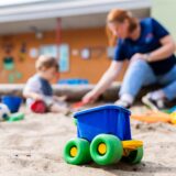 Eine Erzieherin spielt mit einem Kind im Sandkasten einer Kita.