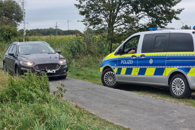 Ein Streifenwagen der Polizei und ein weiteres Auto stehen an einem Feldweg in Gronau-Epe, an dem zwei Leichen gefunden wurden.