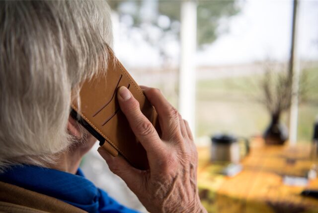 Ein Senior blickt aus dem Fenster und telefoniert mit seinem Handy