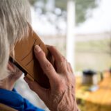 Ein Senior blickt aus dem Fenster und telefoniert mit seinem Handy