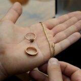Zwei Ringe und eine Kette aus Gold liegen auf der Hand eines Mannes.