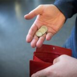Münzen im Wert von fünf Euro werden über ein rotes Portemonnaie gehalten.