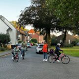 Eine Frau steht mir einer Warnweste bekleidet auf der Straße und achtet darauf, dass Fahrradfahrer sicher abbiegen können.