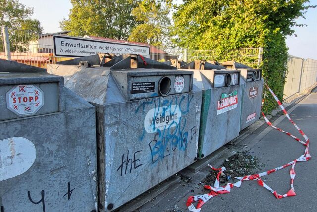 Flatterband und Glasscherben liegen vor einem in Reihe stehenden Altglascontainer.