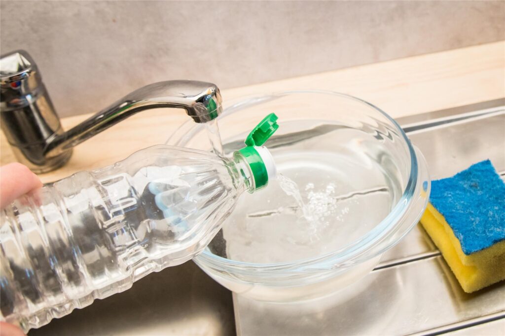 Essig wird in eine Schüssel mit Wasser gegossen. Essig wird in eine Schüssel mit Wasser gegossen.