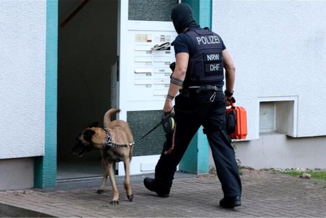 Ein Beamter des Sondereinsatzkommandos betritt mit Hund ein Mehrfamilienhaus.