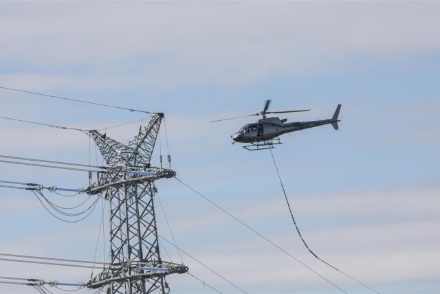 Ein Helikopter fliegt tief an einen Strommaster heran.