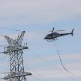 Ein Helikopter fliegt tief an einen Strommaster heran.