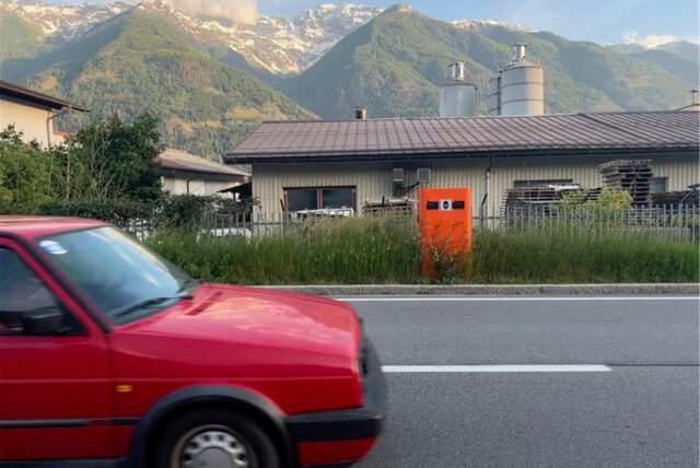 Ein fahrendes Auto vor einer Radaranlage der italienischen Behörden am Rand einer Straße.