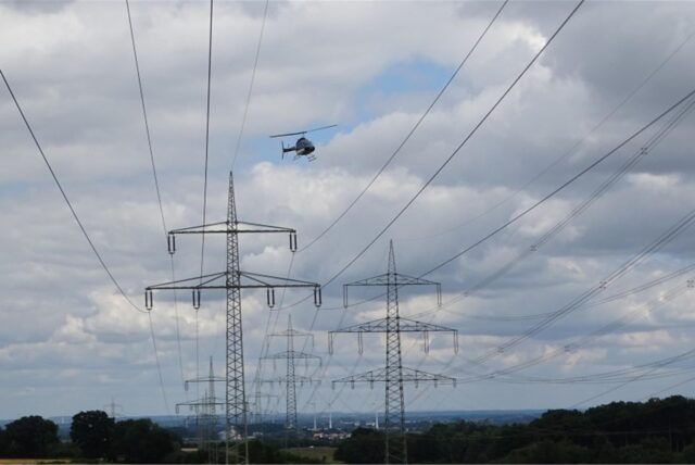 Ein Helikopter fliegt über einer Stromleitung.