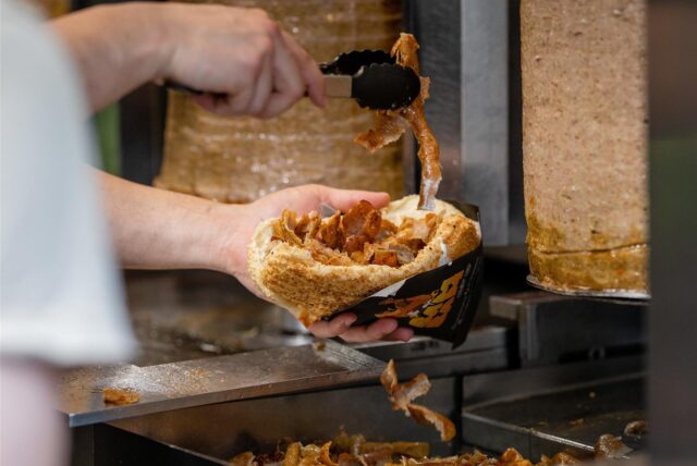 Ein Mitarbeiter einer Dönerbude legt Fleisch in einen Döner
