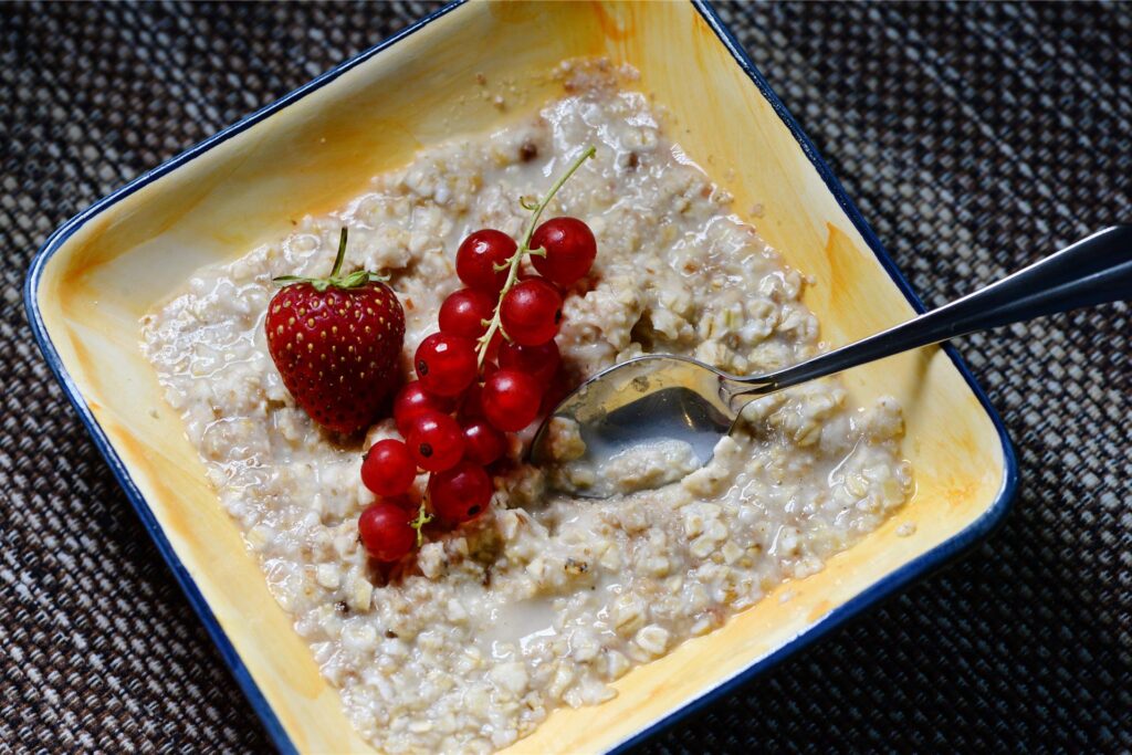 Eine Schale mit Porridge, die mit einer Erdbeere und Johannisbeeren garniert ist, steht auf einem Frühstückstisch.