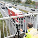 Ein Polizist erfasst das Verkehrsgeschehen auf einer Autobahn von einer Brücke aus mit einer speziellen Kamera