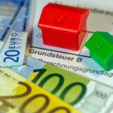 Ein Spielzeughaus und die Nachbildung von Euro-Geldscheinen liegen auf einem Abgabenbescheid für die Entrichtung der Grundsteuer.