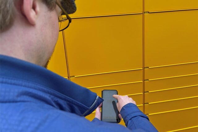 Ein Mann steht vor einer Packstation und betätigt sein Smartphone.