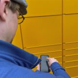 Ein Mann steht vor einer Packstation und betätigt sein Smartphone.