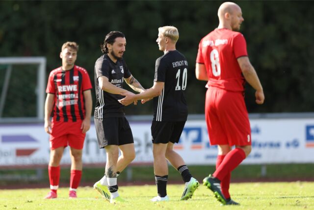 Zwei Spieler in schwarzen Trikots klatschen sich ab. Um sie herum stehen zwei Gegenspieler in roten Trikots.