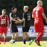 Zwei Spieler in schwarzen Trikots klatschen sich ab. Um sie herum stehen zwei Gegenspieler in roten Trikots.