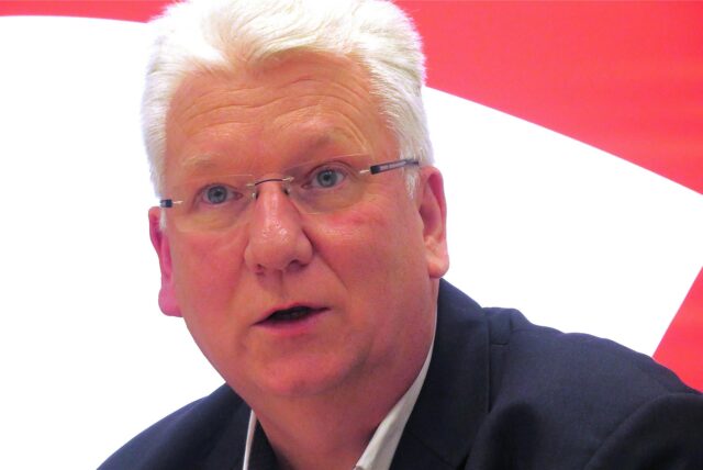 Hartmut Ganzke vor einem rot-weißen Logo der SPD in Unna.