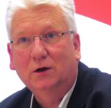 Hartmut Ganzke vor einem rot-weißen Logo der SPD in Unna.