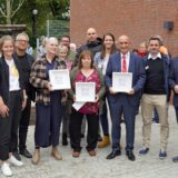 Mehrere Menschen stehen im Halbkreis vor der Kita- und OGS-Neubau an der Schillerschule