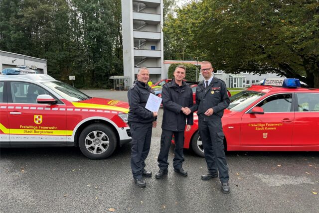 Dirk Kemke (Leiter der Feuerwehr Bergkamen) und Volker Rost (Leiter der Feuerwehr Kamen) stehen mit Tim Krächter vor Feuerwehrfahrzeugen der beiden Städte an der Feuer- und Rettungswache im Mersch und überreichen ihm die Ernennungsurkunde.