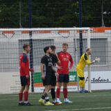 Fußballer in schwarzen und roten Trikots stehen im Strafraum.