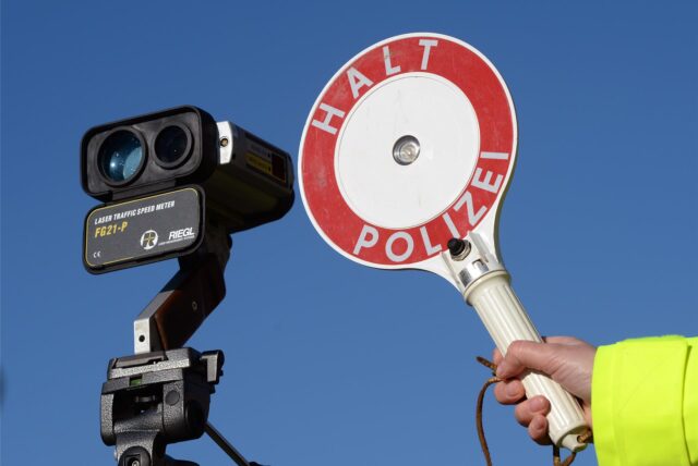 Ein Polizist neben einer Radaranlage hält ein Auto mit einer Polizeikelle an
