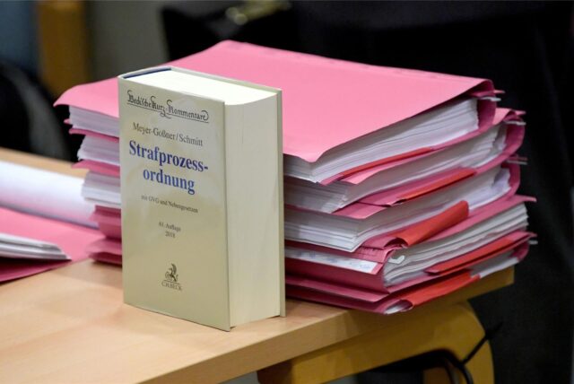 Die Strafprozessordnung steht auf einem Tisch. Dahinter liegt ein Stapel dicker, roter Akten.