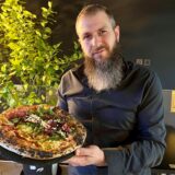 Gastronom Marcel Strozyk vom Pizza-Restaurant „450 Degrees“ in Dortmund-Mengede hält eine Pizza Napoli in die Kamera.