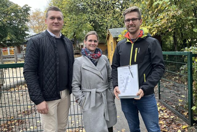 Simon Schulte (v.r.), Gina Schmale und Jan Kiesel stehen vor dem Eingang der Kita und präsentieren die Liste der gesammelten Unterschriften.