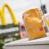 Eine McDonald’s To-Go-Tüte und ein To-Go-Becher stehen vor einer McDonald’s-Filiale.