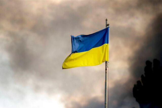 Die ukrainische Flagge ist vor dem Rauch eines Feuers zu sehen, nach Angriffen auf die Ukraine über Kiew. Die Gruppe der sieben großen westlichen Industriestaaten gewährt der Ukraine nach Angaben der US-Regierung einen durch Zinserträge aus eingefrorenem russischen Vermögen abgesicherten Kredit in Höhe von 50 Milliarden US-Dollar (rund 46 Milliarden Euro).