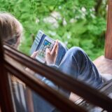 Ein Junge sitzt am Fenster und schaut auf sein Handy.