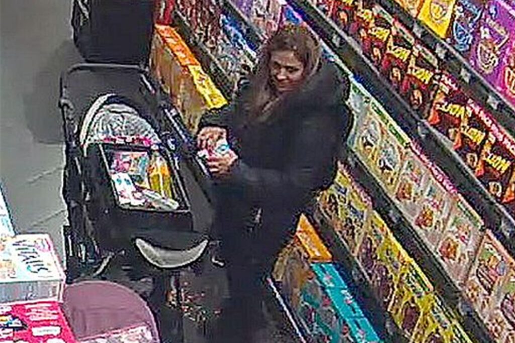 Eine schlanke Frau mit langen dunklen Haaren und einer schwarzen Jacke steht in einem Supermarkt und legt Waren in einen Kinderwagen. Eine schlanke Frau mit langen dunklen Haaren und einer schwarzen Jacke steht in einem Supermarkt und legt Waren in einen Kinderwagen.