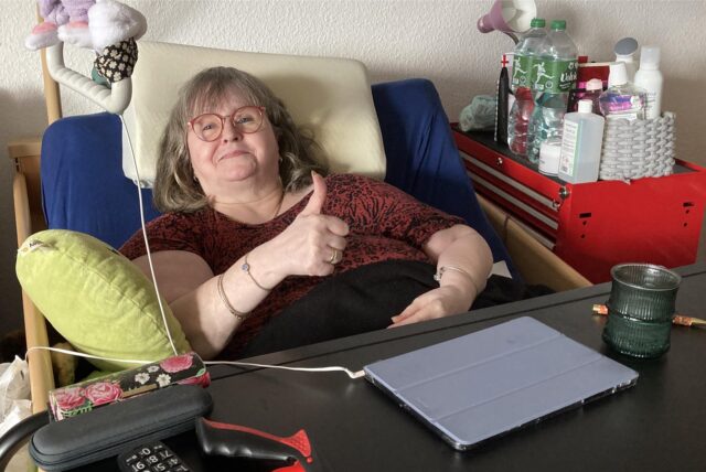 Eine bettlägerige Frau hebt den rechten Daumen.