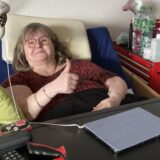 Eine bettlägerige Frau hebt den rechten Daumen.