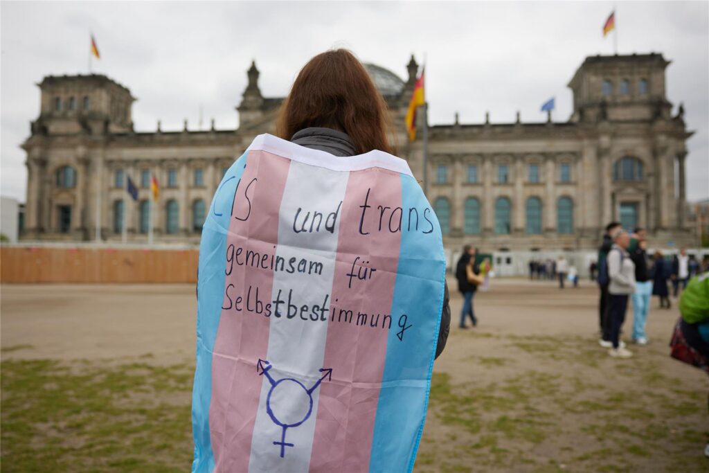 Eine Teilnehmerin steht bei einer Protestveranstaltung gegen das Selbstbestimmungsgesetz von Frauengruppen mit einer Transgender-Pride-Flagge vor dem Bundestag.