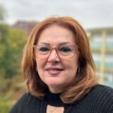 Liliana Roth lehnt an einem Geländer und schaut in die Kamera