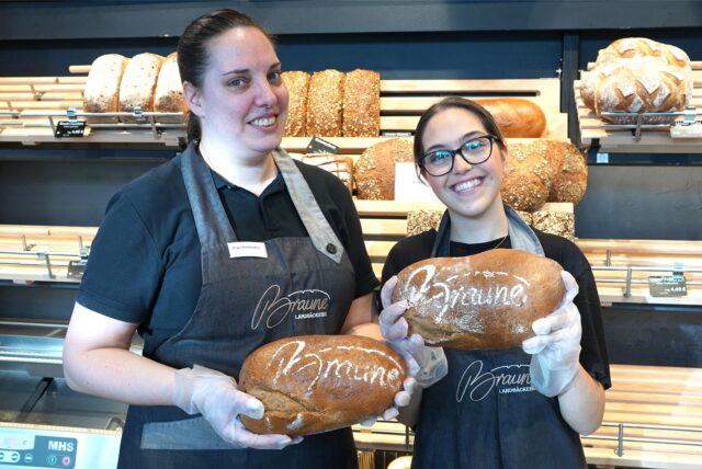 Zwei Bäckereifachverkäuferinnen lächeln in die Kamera und halten Brote in den Händen.