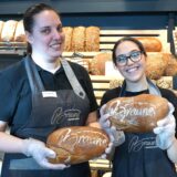 Zwei Bäckereifachverkäuferinnen lächeln in die Kamera und halten Brote in den Händen.
