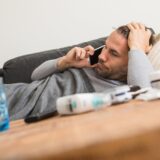 Ein Mann liegt erkrankt auf einem Sofa und telefoniert.