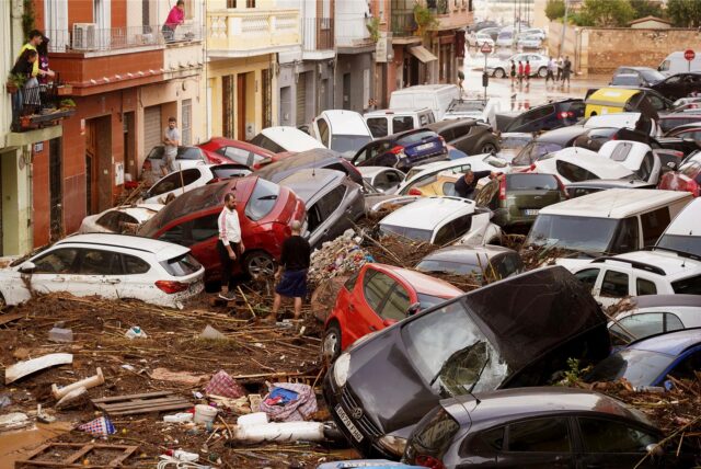 Anwohner betrachten durch die Wassermassen aufgestapelte Autos nach dem fürchterlichen Unwetter in Spanien.