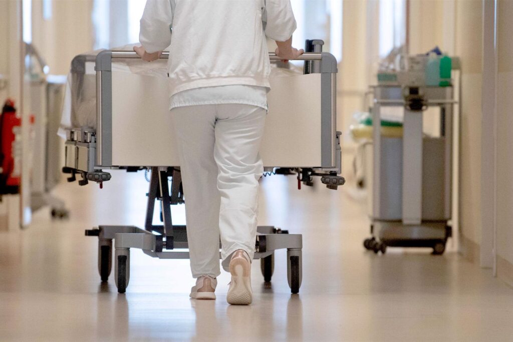 Eine Krankenpflegerin schiebt ein Krankenbett durch einen Krankenhausflur. 